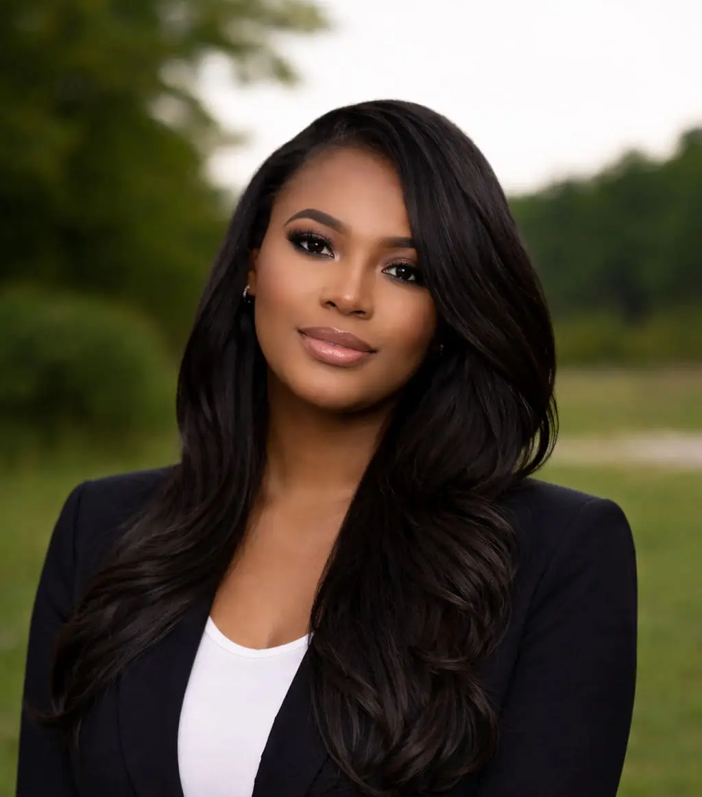 Professional woman outdoors in a park, wearing a black blazer and white top, looking at the camera with a slight smile.